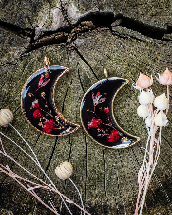Two moon shaped resin dog tags with black background and red flowers.